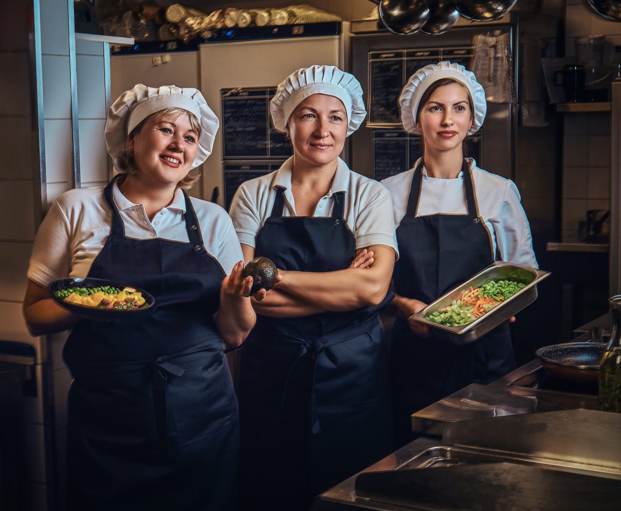 cooking team standing next to a table with chopped vegetables at restaurant s kitchen